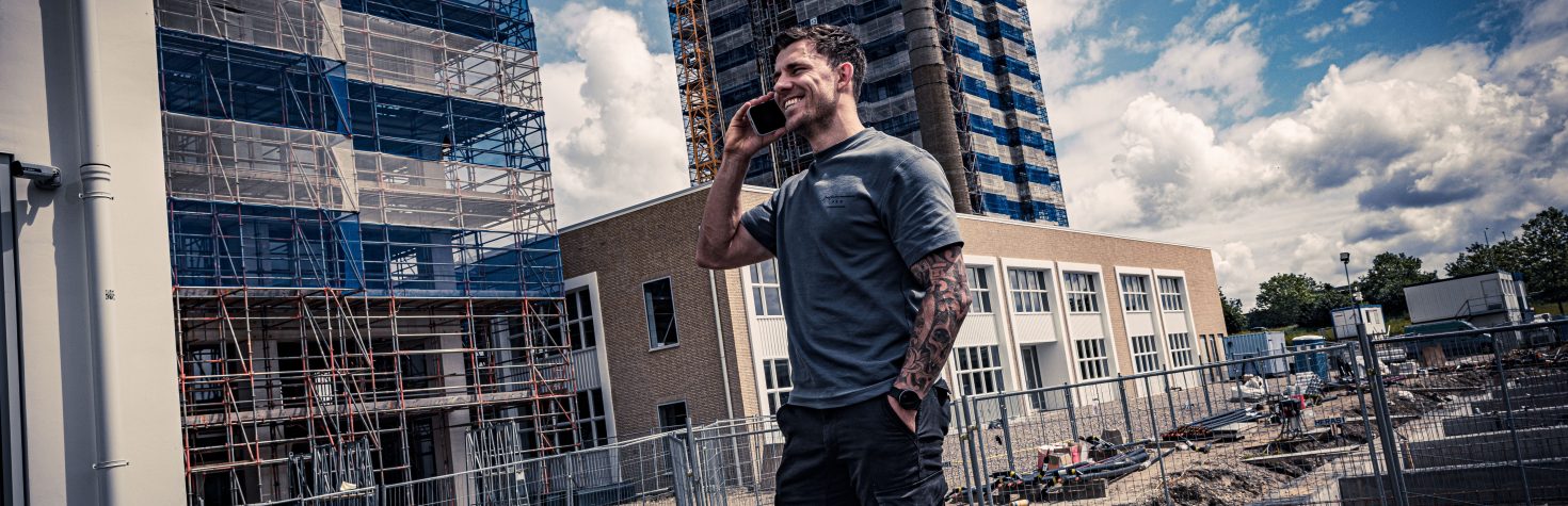 Man belt op een bouwterrein met steigerwerk en hoge gebouwen op de achtergrond.