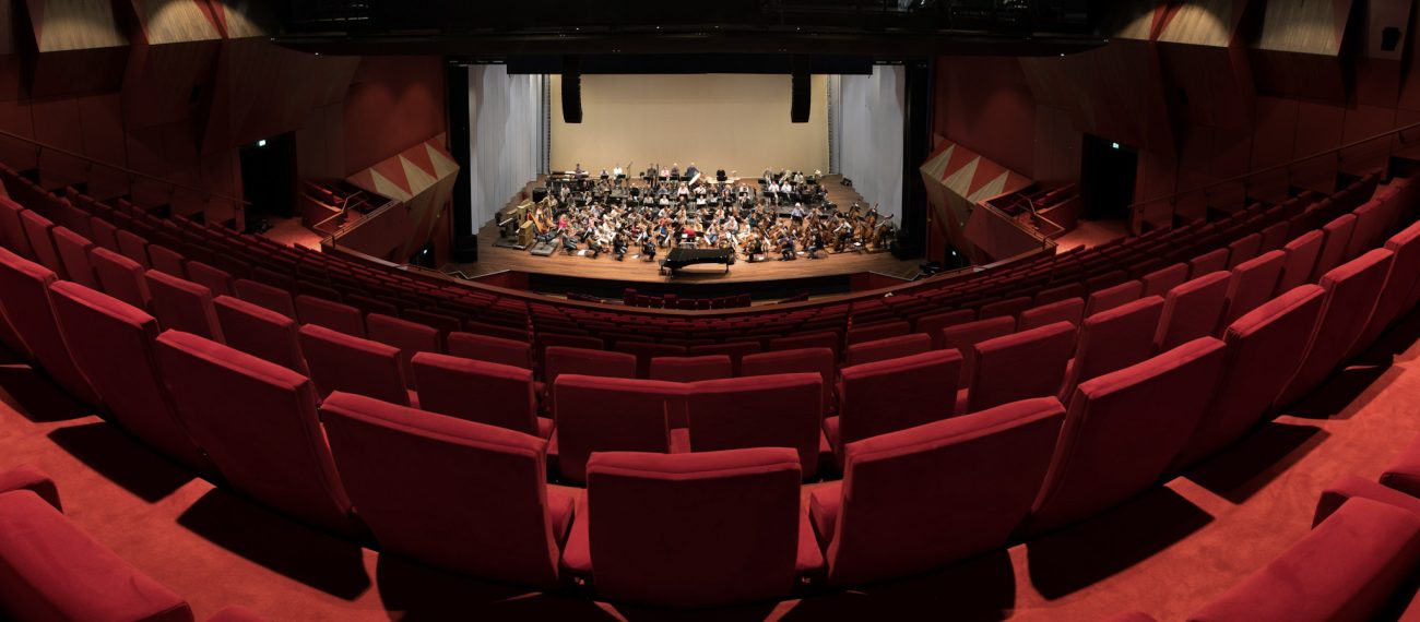 Verbouwing Theater aan het Vrijthof: panorama rode tribunes richting podium met orkest en vleugel