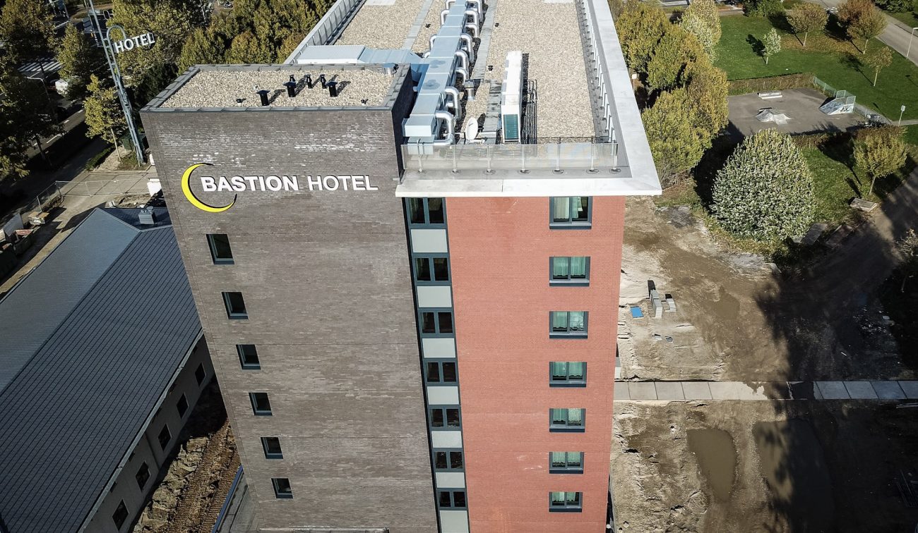 Bastion Hotel Geleen – luchtfoto van dak met installaties, logo op zijgevel en rood-bakstenen kopgevel, terrein in aanleg