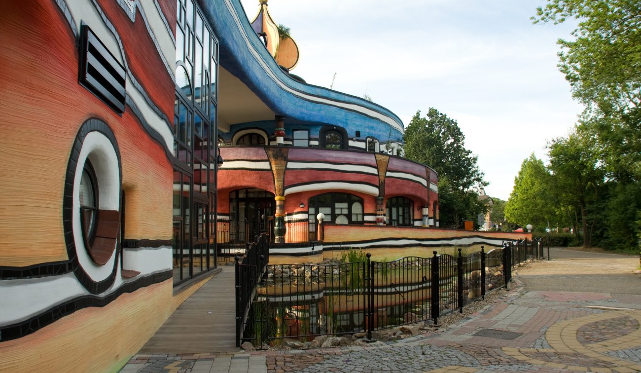 Ronald McDonald Kindervallei in Valkenburg met golvende blauw-rode gevel, loopbrug en vijver met hekwerk aan de voorzijde.
