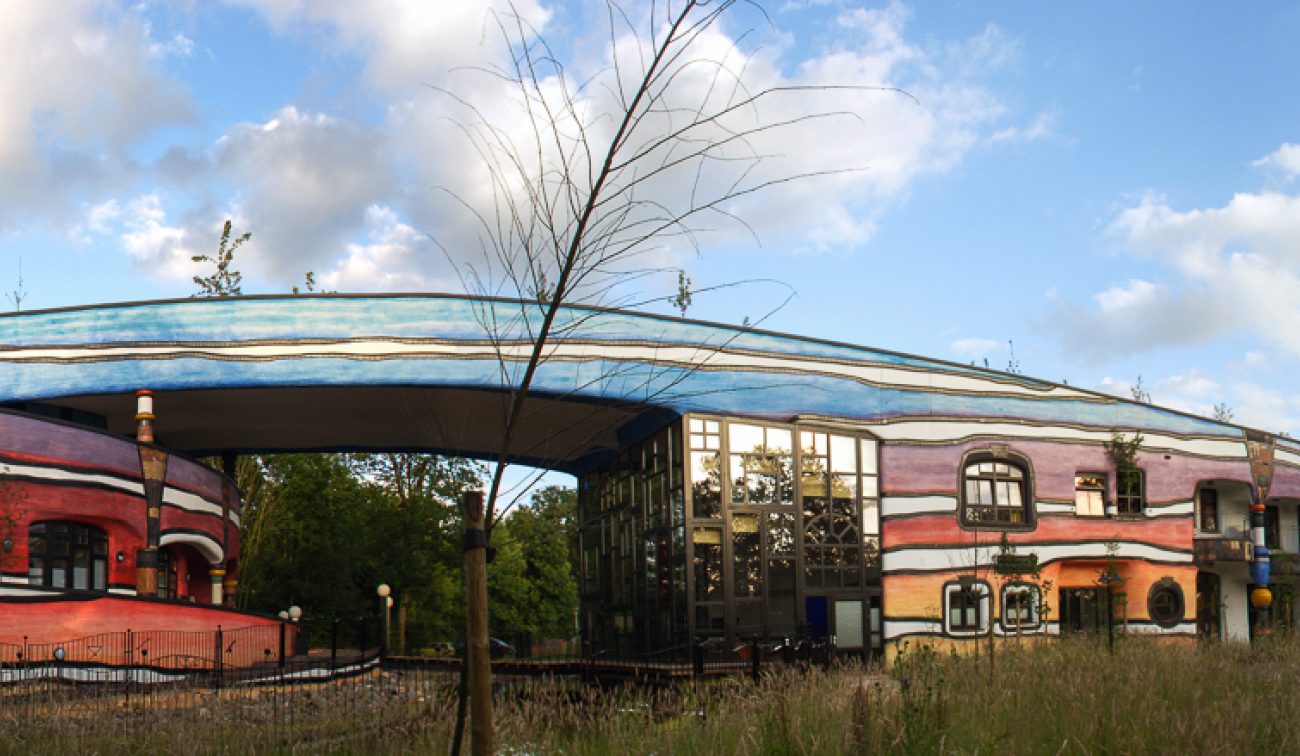 Panoramafoto van de Ronald McDonald Kindervallei in Valkenburg: kleurrige Hundertwasser-architectuur met ronde toren, goudkleurige koepel en brede blauwe boog.