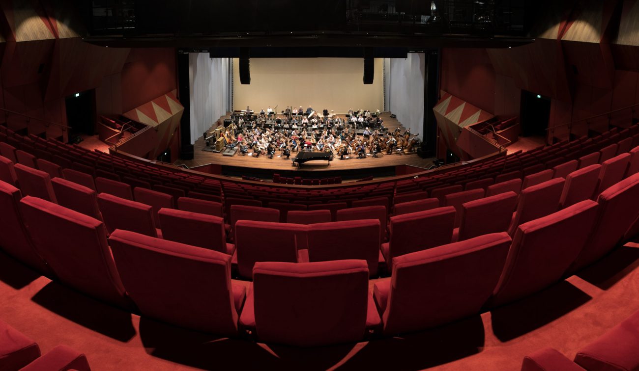 Verbouwing Theater aan het Vrijthof: panorama rode tribunes richting podium met orkest en vleugel