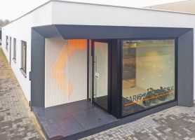 Hoekentree van gerenoveerd kantoor Caris & Reiner in Sittard met zwart kader, glazen pui en geperforeerde wand met oranje verlichting op een donkere tegelopstap.