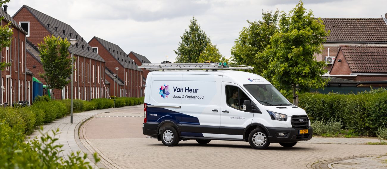 Bedrijfsbus van Van Heur Bouw & Onderhoud rijdt door een woonwijk met nieuwbouwwoningen.