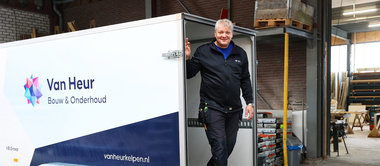 Medewerker stapt uit bedrijfsaanhanger met oprijplaat in werkplaatsomgeving, met logo van Van Heur Bouw & Onderhoud op de zijkant.”