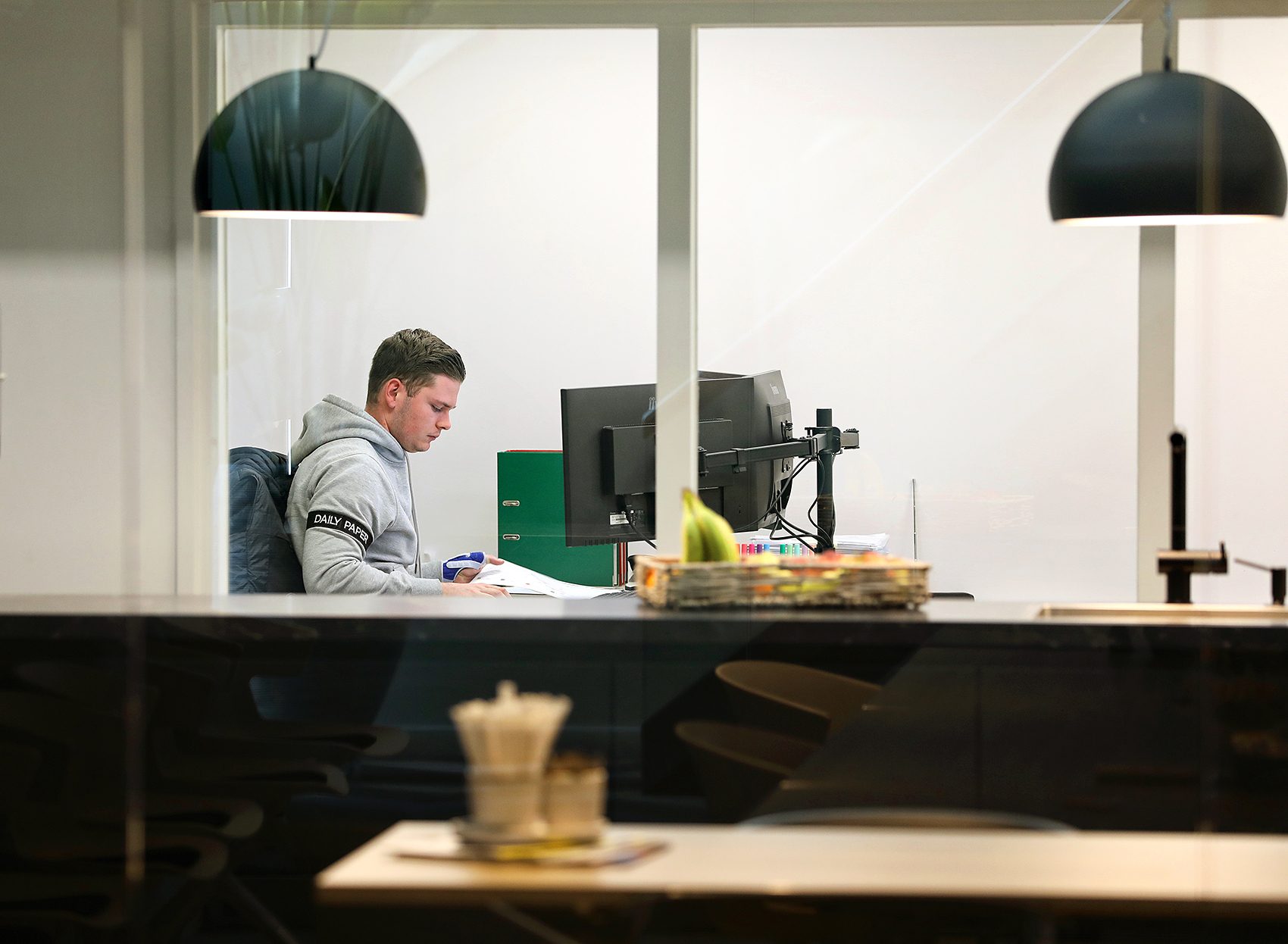 Medewerker werkt geconcentreerd aan documenten achter een computerscherm in een afgesloten kantoorruimte.