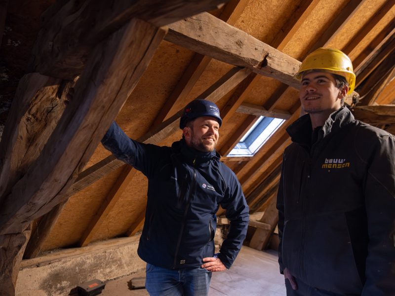 Bouwmedewerkers inspecteren houten dakconstructie op zolder.