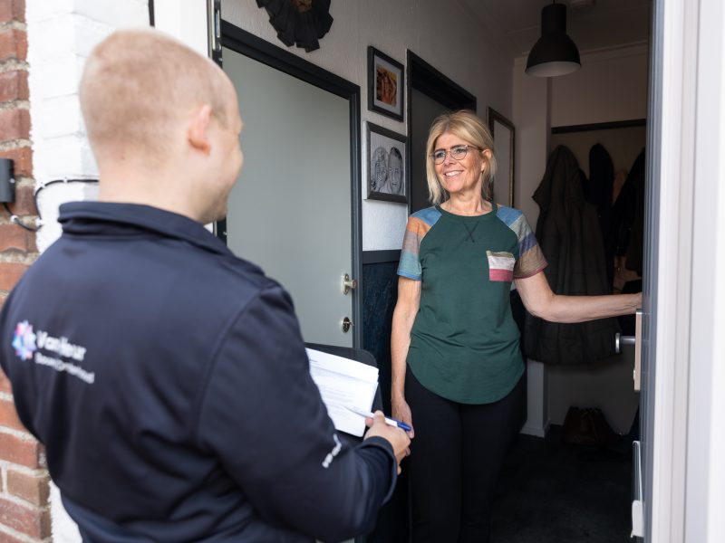 Monteur aan de deur in gesprek met bewoner bij binnenkomst voor woningservice.