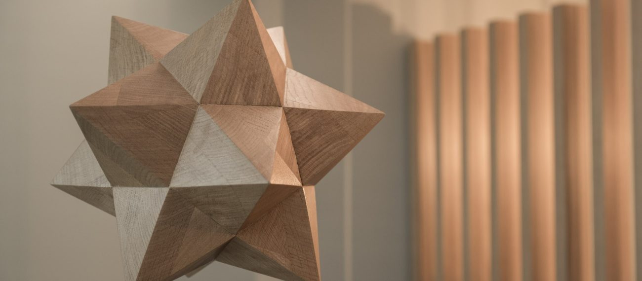 Abstract houten kunstobject met geometrische vormen, tentoongesteld in modern interieur met warme verlichting.
