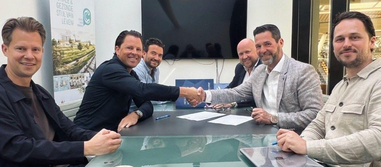 Vijf mannen schudden elkaar de hand tijdens een zakelijke bijeenkomst aan tafel.