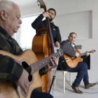 Drie muzikanten spelen gitaar en contrabas in een lichte ruimte.