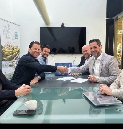 Vijf mannen schudden elkaar de hand tijdens een zakelijke bijeenkomst aan tafel.