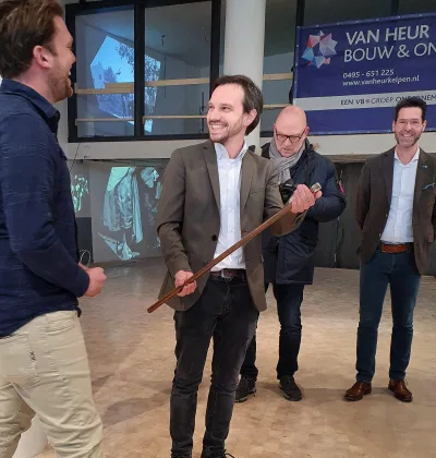 Openingshandeling met houten voorwerp tijdens bijeenkomst van Van Heur Bouw & Ontwikkeling