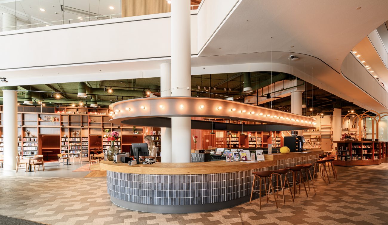Moderne ontvangstzone met tegelbalie, brochures en open boekenkastruimte.