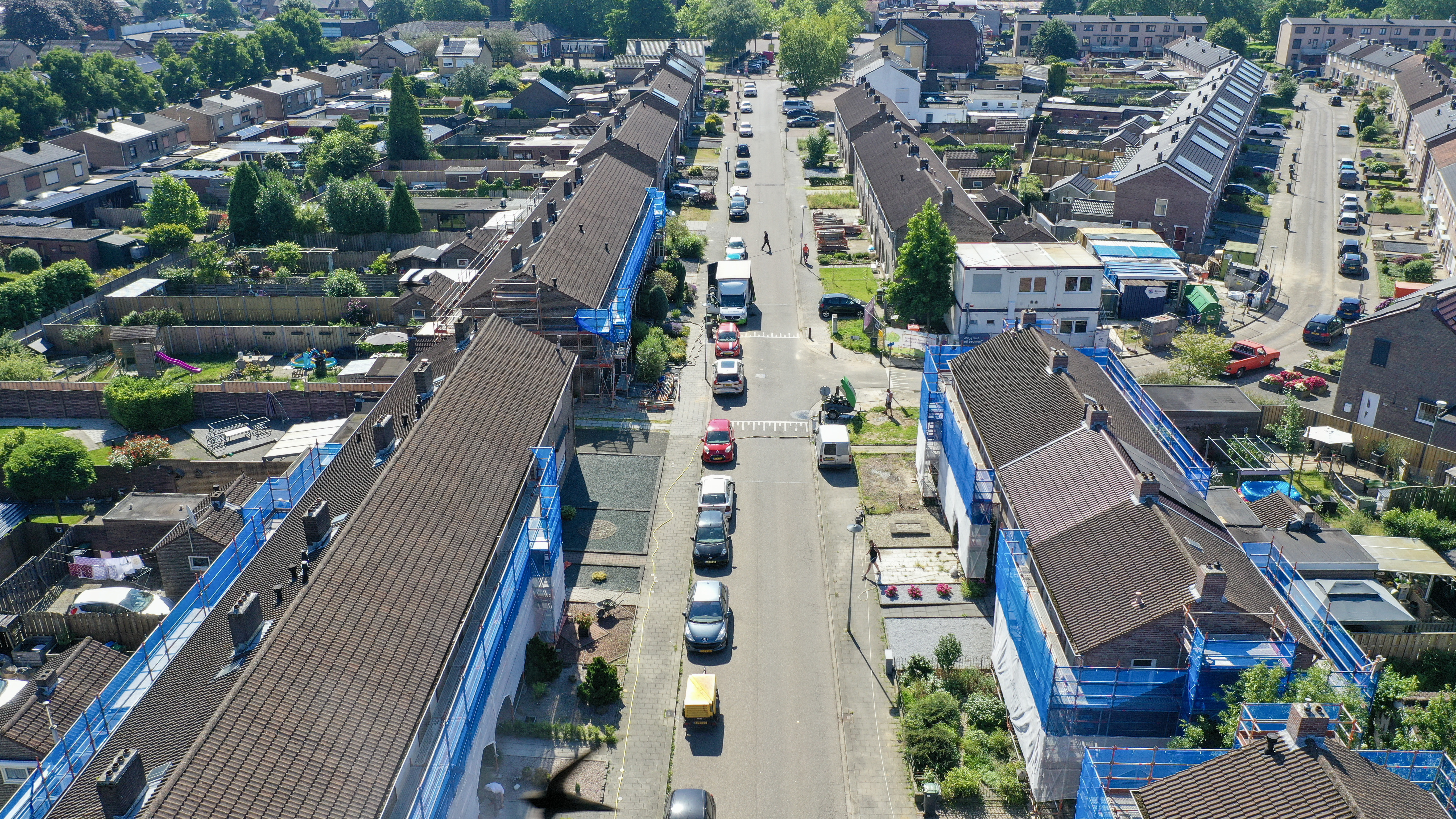 Luchtperspectief straat met aaneengesloten woningen in onderhoud, werkbusjes en hekken — Groot onderhoud 154 woningen Nieuwdorp Stein