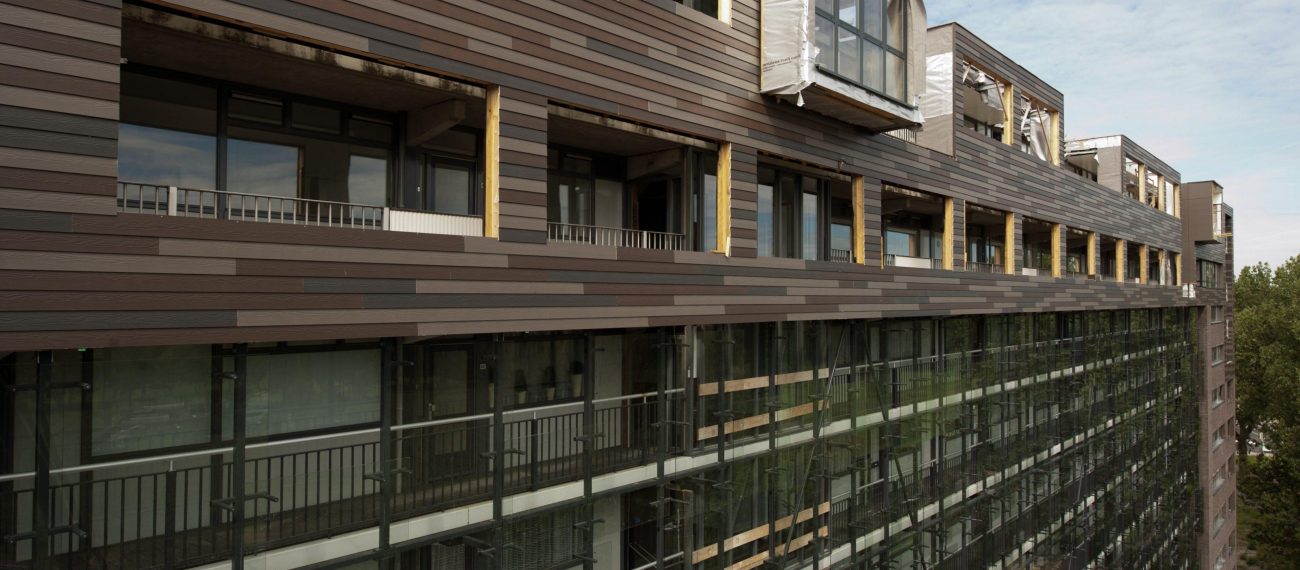 Gerenoveerd appartementencomplex met moderne gevelbekleding in horizontale houttinten en grote ramen, met enkele units zichtbaar in verbouwing onder een bewolkte lucht.