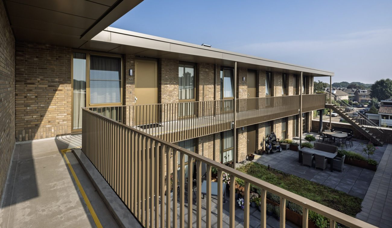 De Scheperij Teteringen: galerijwoningen met binnentuin zitplekken, plantenbakken en baksteengevels.