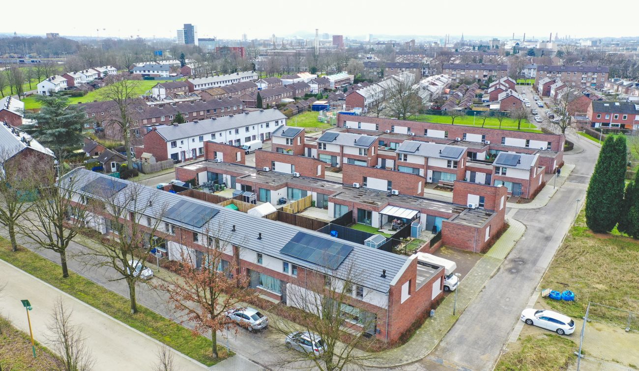 Luchtfoto van nieuwbouwproject met 28 grondgebonden woningen in Nazareth, Maastricht: bakstenen rijwoningen met platte daken, deels voorzien van zonnepanelen, rondom smalle straten en achtertuinen.