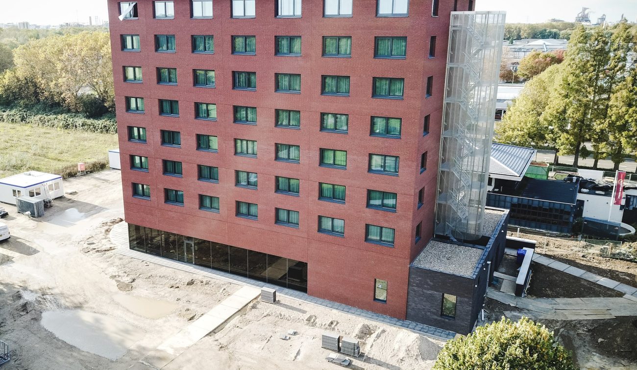 Nieuwbouw Bastion Hotel Geleen – luchtfoto van rood bakstenen hotel met glazen trappenhuis en glazen plint, terrein in afbouwfase