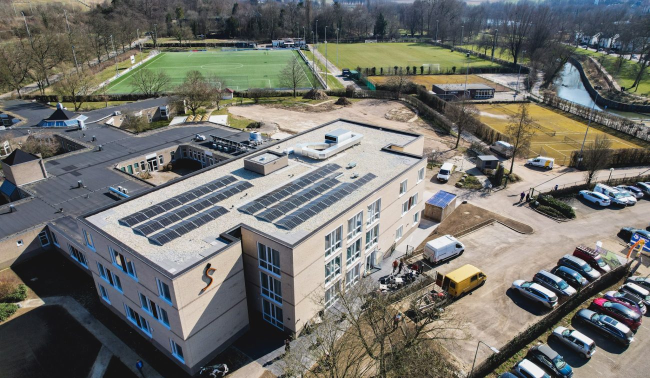 Luchtfoto zorgcomplex Valkenheim Valkenburg met zonnepanelen op dak en sportvelden ernaast.