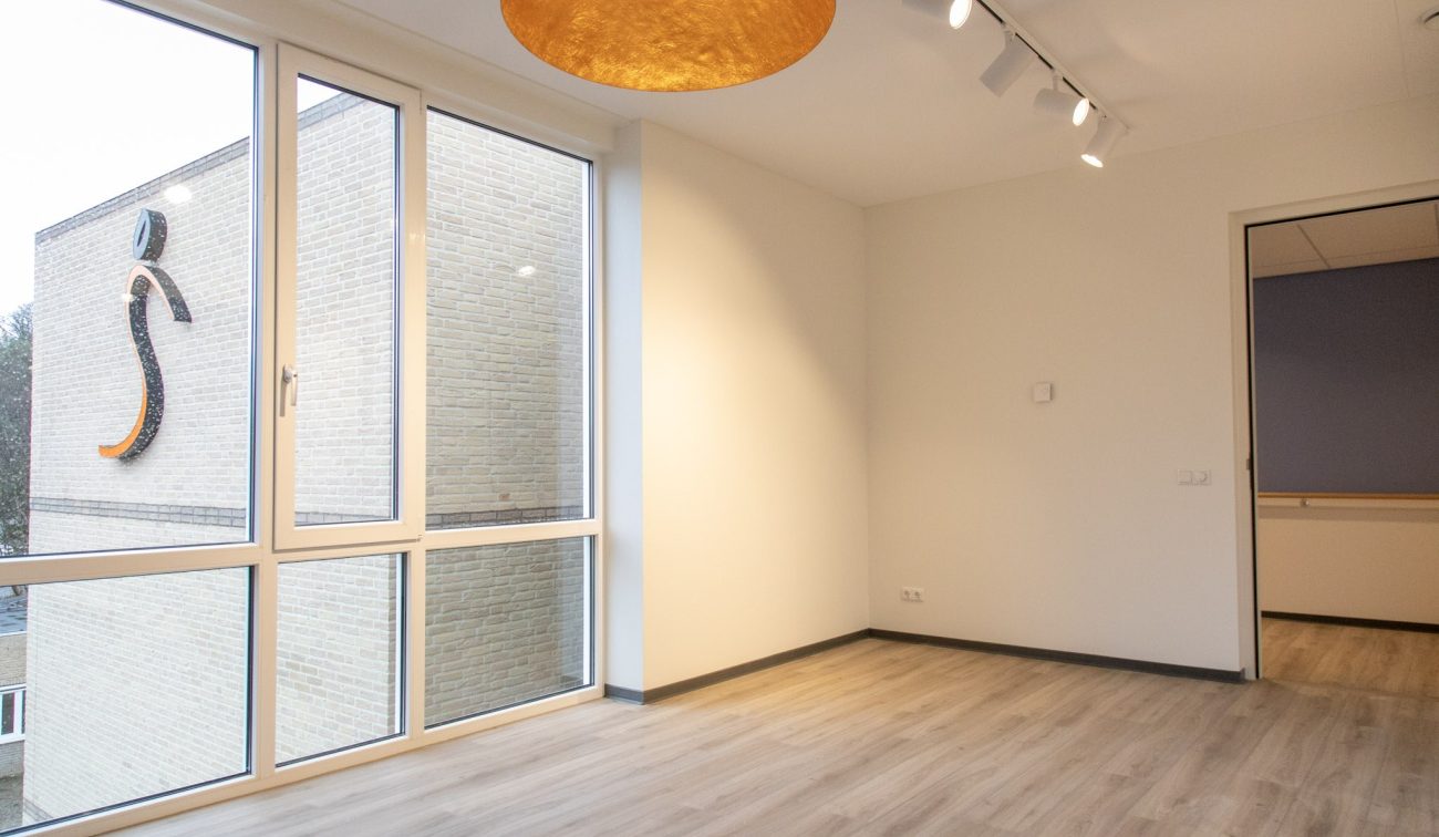 Interieur nieuwbouw Valkenheim, witte wanden, spotrails en raampartij met S-logo buiten.