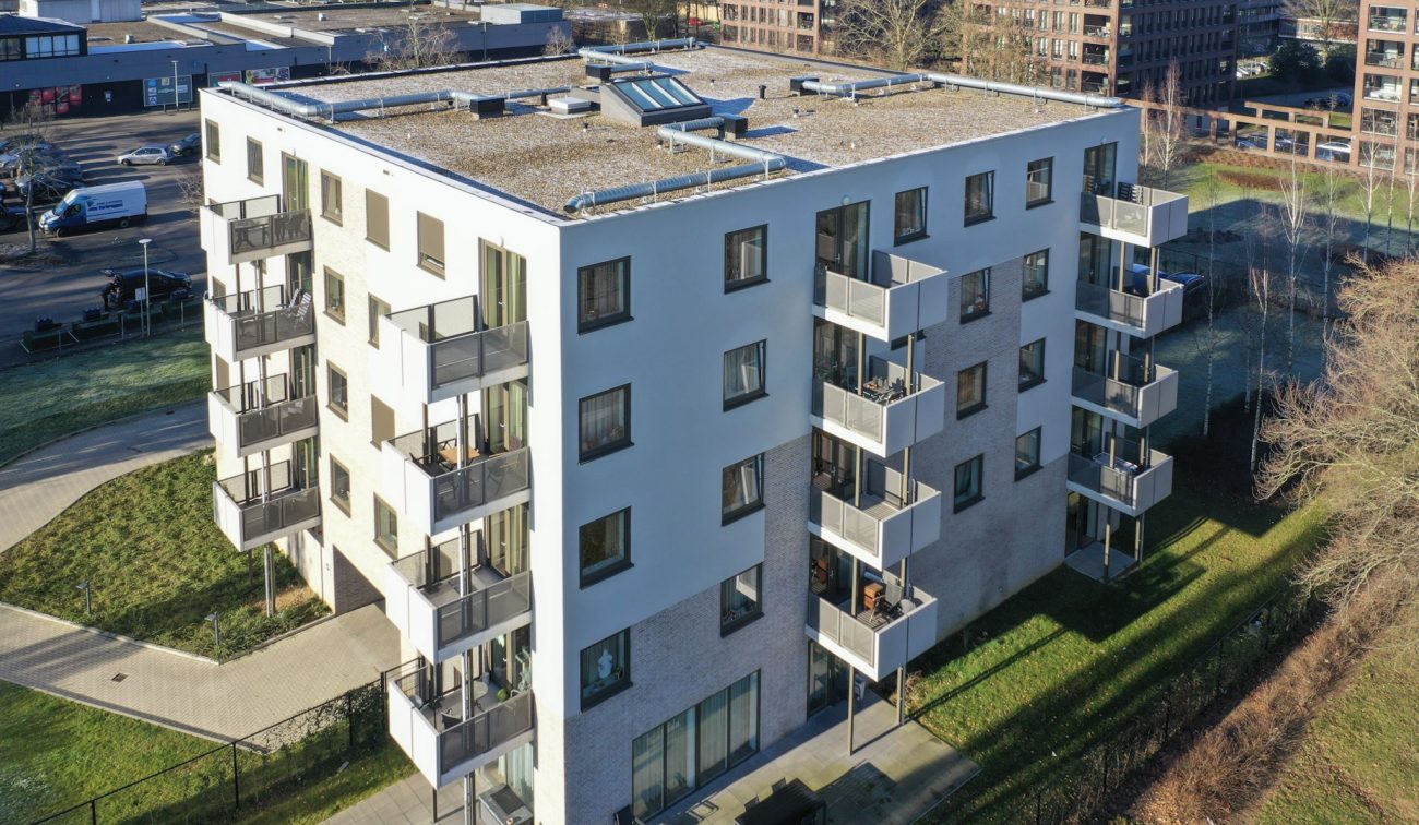 Nieuwbouw Noorderkroon Brunssum – modern vijflaags appartementengebouw met hoekbalkons, witte gevel en bakstenen plint, plat dak met installaties