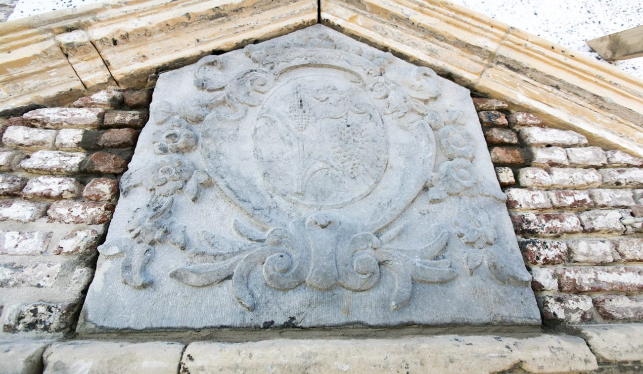 Natuurstenen gevelsteen met wapenschild en barok ornament boven bakstenen topgevel — Herbestemming hoeve tot appartementen Maastricht