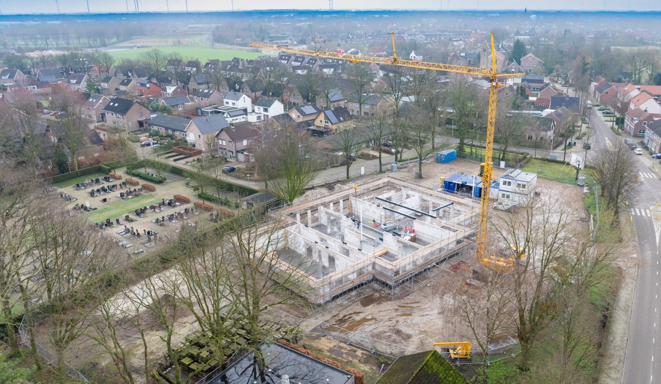 Nieuwbouw Antoniusschool Zundert: dronefoto ruwbouw met steigers, kraan en betonwanden tussen bomen.
