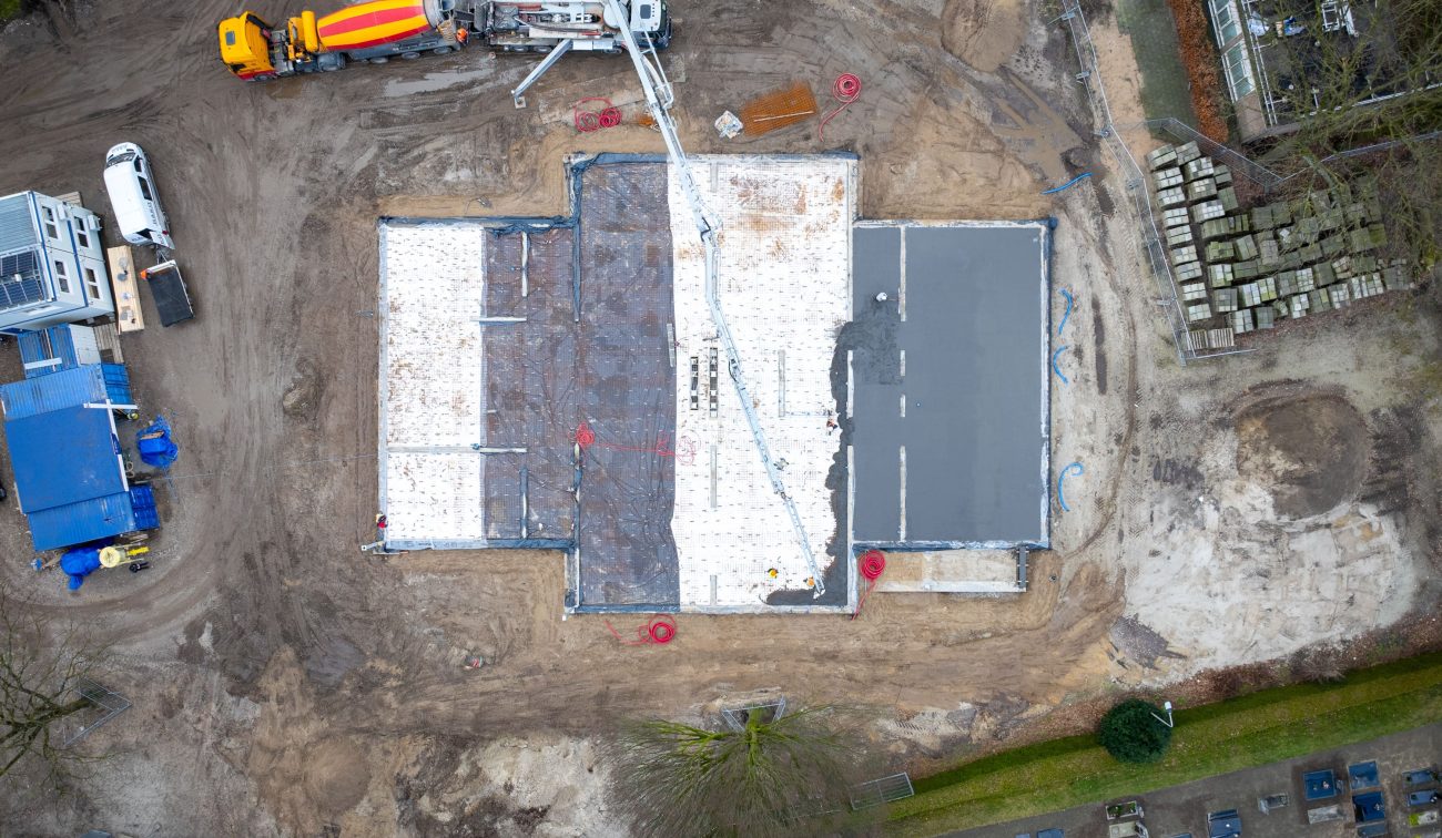 Antoniusschool Zundert: dronefoto stort fundering met betonpomp, mixerwagens en bekisting op terrein