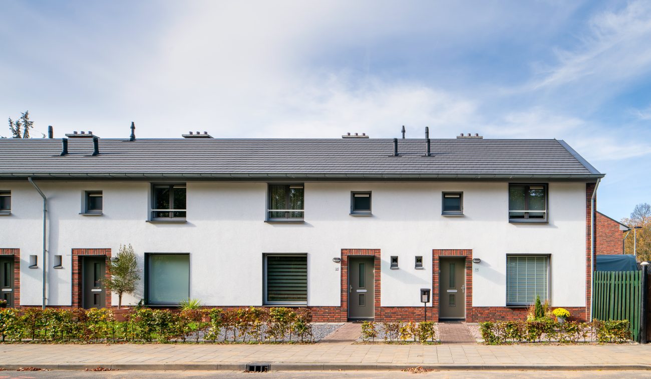 Rij eengezinswoningen met witte gevel en baksteenaccenten, grijs pannendak en kleine voortuinen langs de stoep in wijk Nazareth (Maastricht).