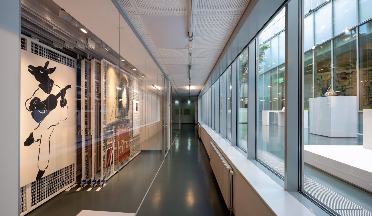 Glastunnel bij SCHUNCK Heerlen met schuifbare kunstracks links en grote ramen rechts met zicht op het lichte atrium met vitrines.