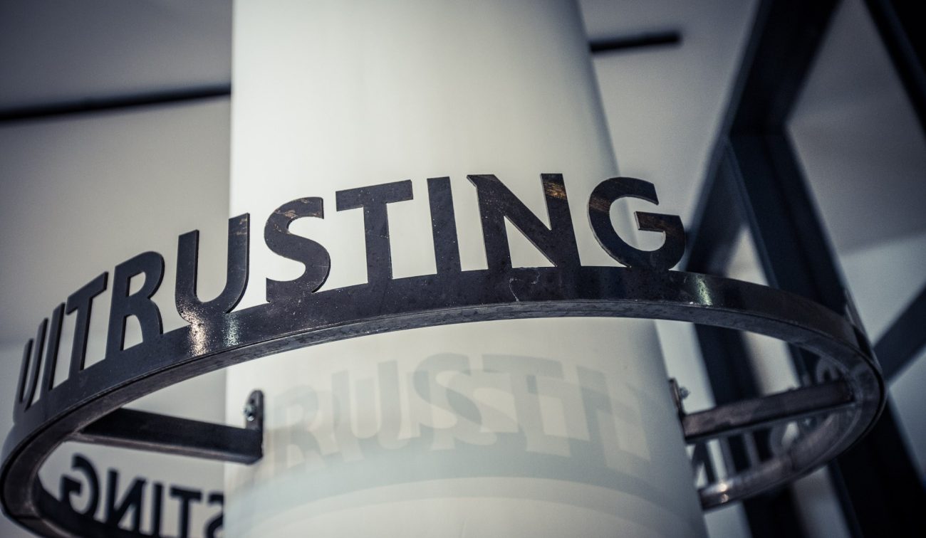 Close-up van een metalen ring met uitgesneden letters ‘TRUSTING’, bevestigd rond een witte kolom in het Nederlands Mijnmuseum.
