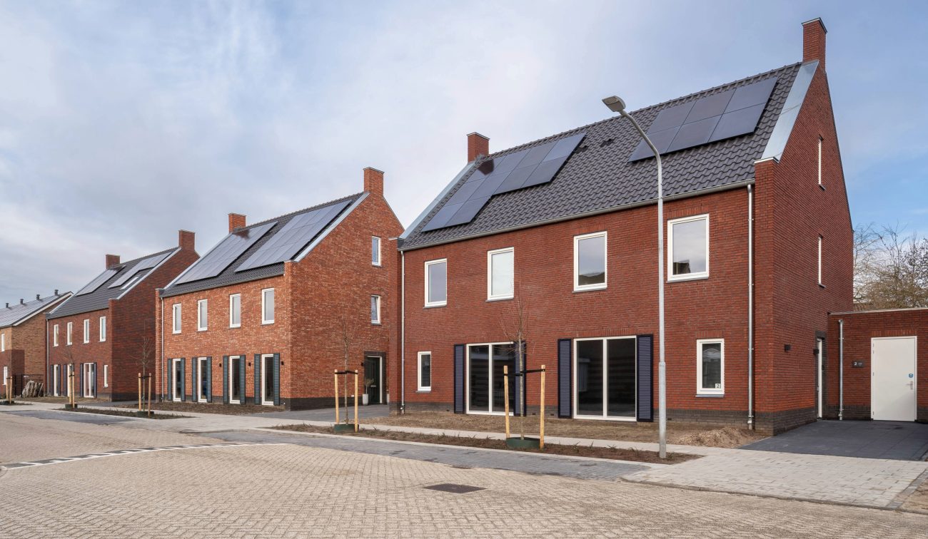 Rijtjeswoningen met bakstenen gevels, zonnepanelen en brede straat in nieuwbouwwijk