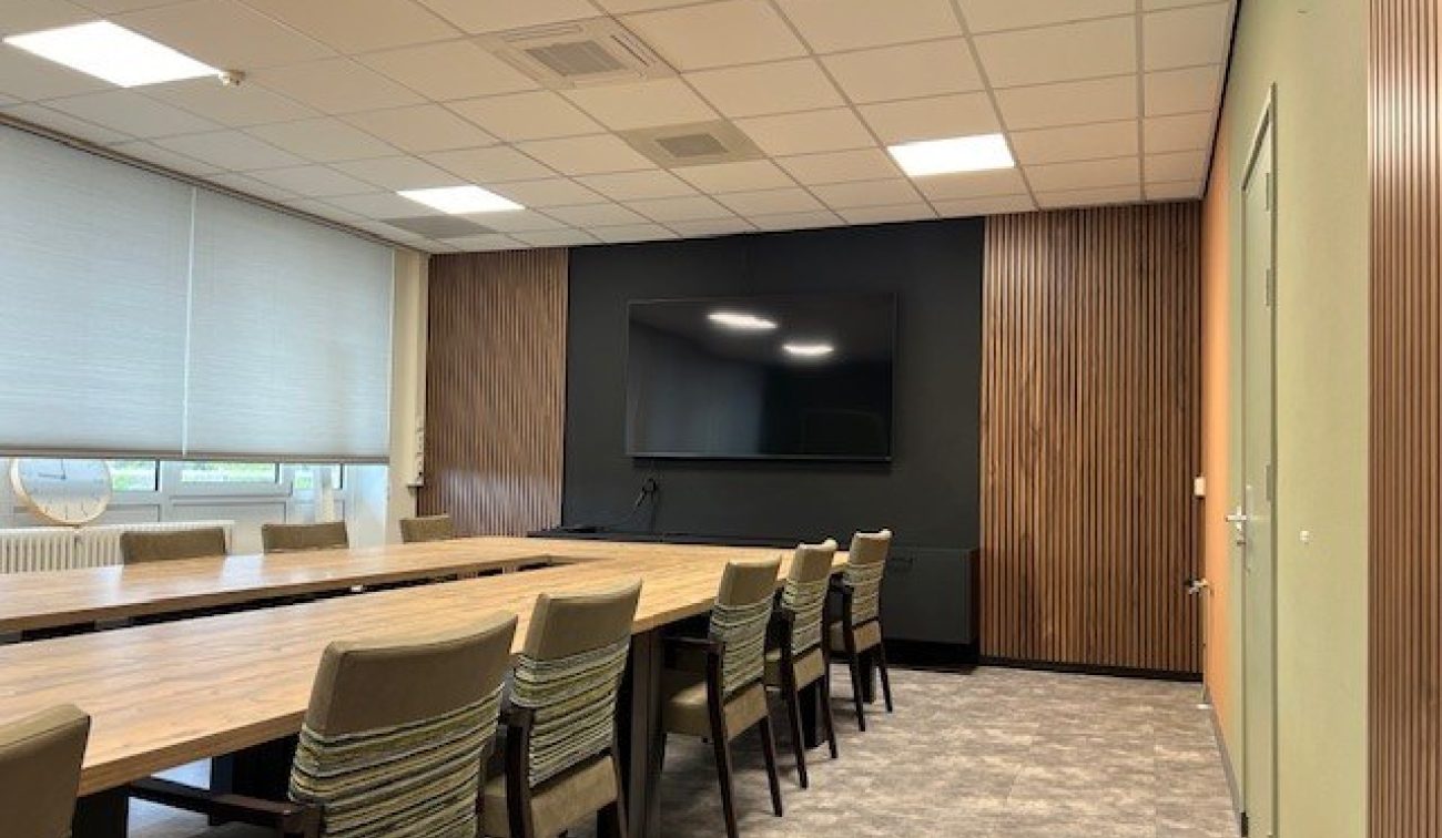 Renovatie zorgcentrum Schuttershof Brunssum – vergaderruimte met houtlattenwand, groot scherm en lange tafels