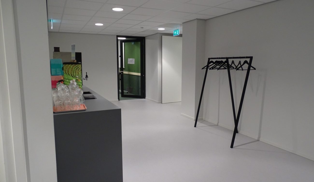 Foyer met zwarte buffetbalie, glazen karaffen, open deur naar groene gang en losse kapstok met hangers