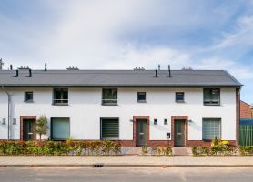 Rij eengezinswoningen met witte gevel en baksteenaccenten, grijs pannendak en kleine voortuinen langs de stoep in wijk Nazareth (Maastricht).