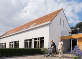 Impressie transformatie oude school Buchten: wit stuc, oranjerood pannendak en tuin met paarse beplanting