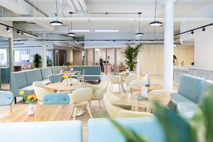 Lichte ontmoetingsruimte met ronde tafels, pastelkleurige stoelen en planten.