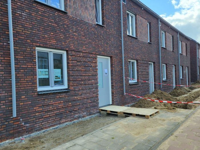 Nieuwbouw Bredeweg Roermond – bakstenen rijwoningen met grijze deuren en ramen, graafwerk langs gevel en tijdelijke loopplank