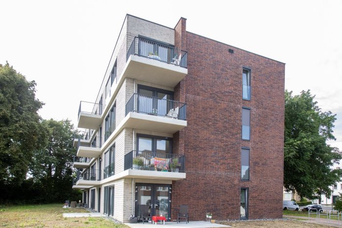 Hoekaanzicht nieuwbouw sociale huurappartementen Margraten met balkons en roodbruine zijgevel.