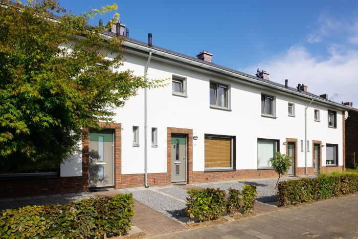 Gerenoveerde rijtjeswoningen met witte gevels en baksteenaccenten, grijze deuren en kozijnen. Voortuinen met grind en lage hagen; boom links in beeld op een zonnige dag.