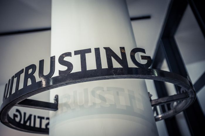 Close-up van een metalen ring met uitgesneden letters ‘TRUSTING’, bevestigd rond een witte kolom in het Nederlands Mijnmuseum.