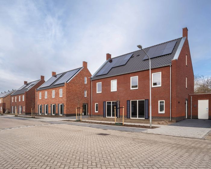 Rijtjeswoningen met bakstenen gevels, zonnepanelen en brede straat in nieuwbouwwijk