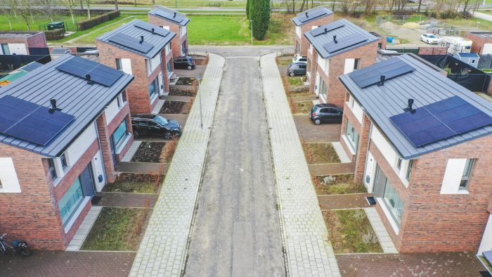 Luchtfoto van een smalle straat tussen nieuwe rijwoningen in Nazareth (Maastricht); bakstenen gevels met grote ramen, daken vol zonnepanelen, kleine voortuinen en geparkeerde auto’s langs het trottoir.