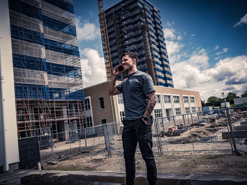Man belt op een bouwterrein met steigerwerk en hoge gebouwen op de achtergrond.